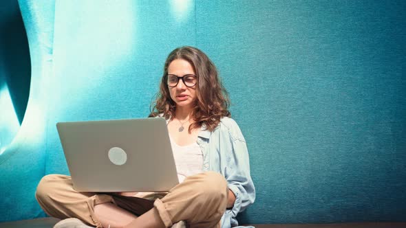 A Young Woman Wearing Glasses Leading a Video Call with Colleagues on Her Laptop