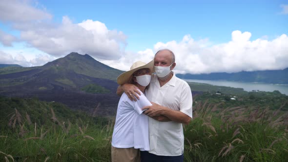 Portrait of Middleaged Couple in Face Masks Hugging in Front of Mountains and Ocean