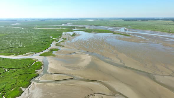 Aerial shot of narrow rivers winding through beautiful green wetlands and river banks under a blue s