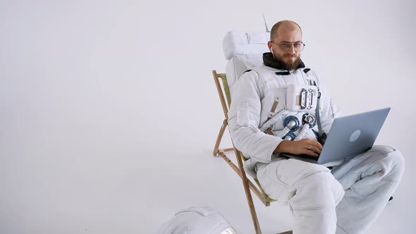 Astronaut with Glasses Sits in a Chair Works with a Laptop on His Lap