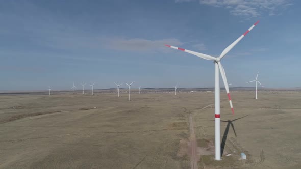 Blades of a Large Wind Turbine in a Field Against a Background of Cloudy Blue Sky on the Horizon