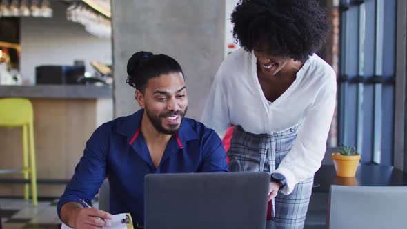 Diverse couple sitting at a table in a cafe using laptop smiling and talking