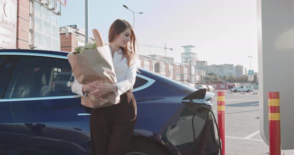 Beautiful Business Woman Stands Near Her Electric Car With Groceries