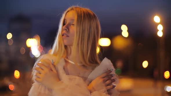 Attractive and Tender Caucasian Teenage Girl Hugs Herself in the City at Night on a Background of