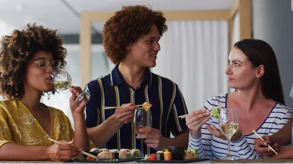 Diverse group of happy friends drinking wine eating sushi and talking at a bar