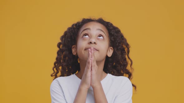 Cute Little African American Girl Praying to God Looking Upward and Making Wish Orange Background