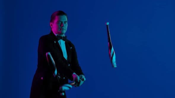 Stylish Showman Juggles Pins in a Dark Studio