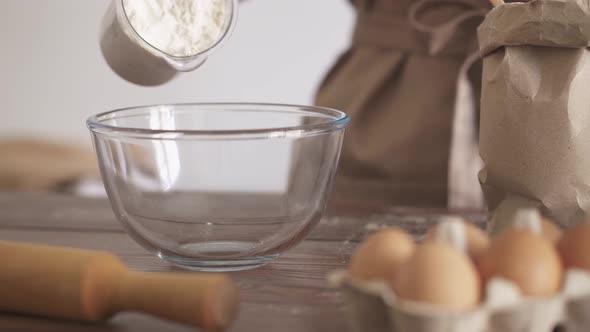 Kneading The Dough. The Chef Pours The Flour From A Measuring Glass Into A Transparent Bowl