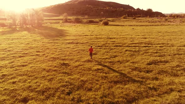 Flight Over Sport Man at Perfect Green Grass Meadow. Sunset in Mountain