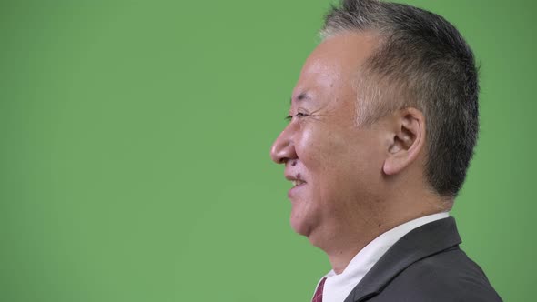 Profile View of Mature Japanese Businessman Smiling Against Green Background