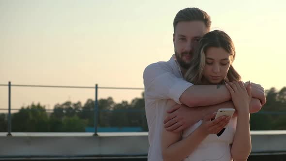 Happy woman and man are standing on roof together and hugging in evening