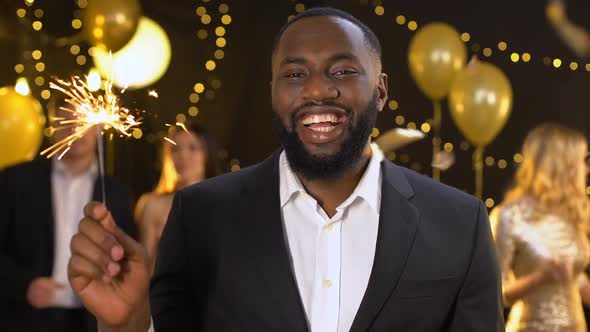 Joyful Black Male Holding Bengal Light in Hand Smiling Camera Festive Event