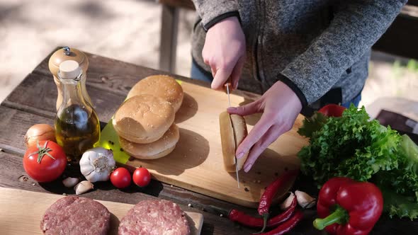 Woman Cut in a Half Hamburger Bun with a Knife on a Wooden Board Outdoors