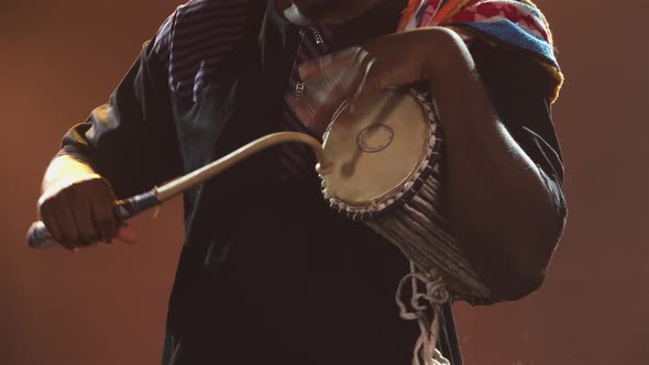 Black Musician Plays Talking African Yuka Drum in a Dark Studio Against a Backdrop of Bright Lights