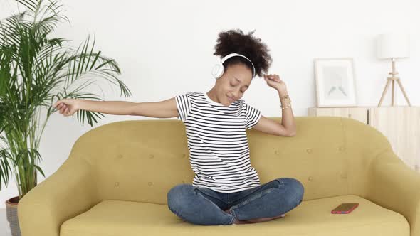 Happy Young Woman Listening to Music While Dancing Sitting on Sofa at Home