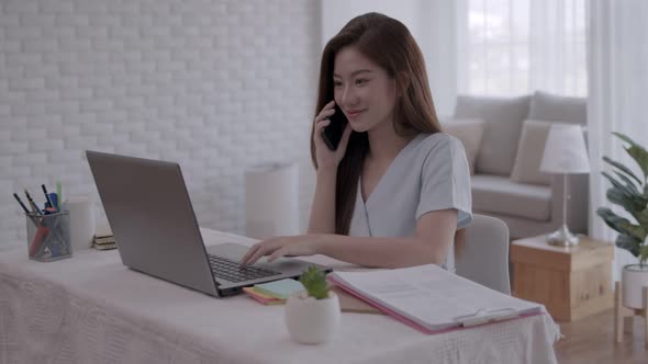 Business Asian woman Talk to work on the phone and take notes on the laptop with work from home.