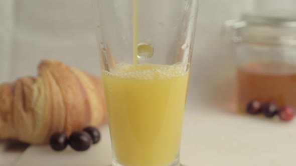 Pouring fresh orange juice at breakfast with honey and croissants