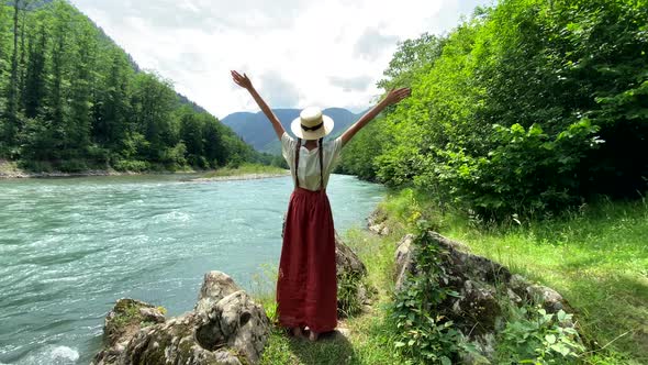 Young beautiful romantic vintage woman in straw hat going to stone coast near mountain river, travel