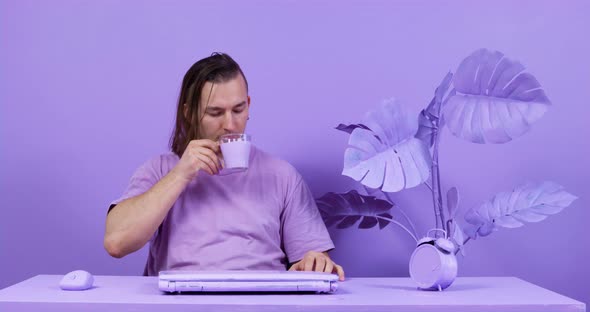 Tired Man Drinks Milk Sitting at Table Near Closed Laptop