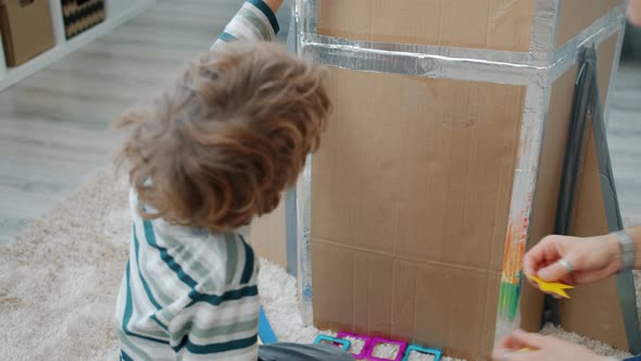 Child and Mother Decorating Cardboard Spaceship with Colorful Stickers Playing at Home