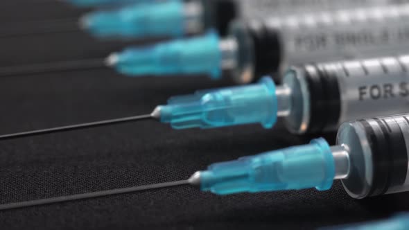 A Lot of White Transparent Syringes with Needle Lie on Black Table. Close-up Macro Footage of