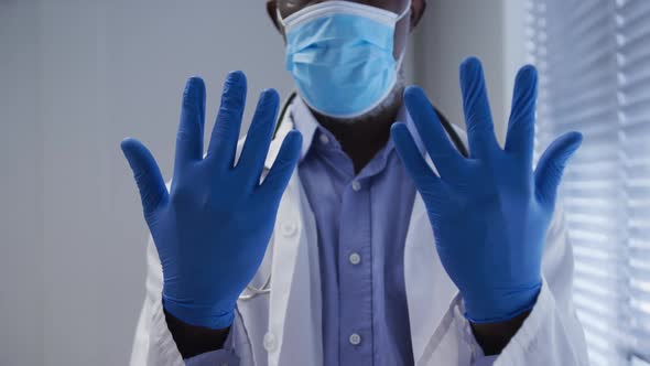 Midsection of mixed race male doctor wearing face mask and surgical gloves