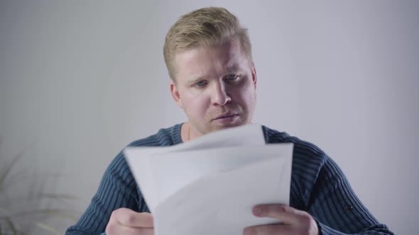 Close-up of Dissatisfied Caucasian Man Looking Through Documents and Throwing Them Away. Annoyed