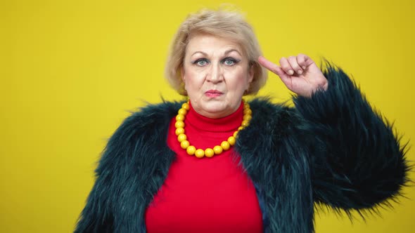 Portrait of Annoyed Irritated Senior Woman Showing Nuts Gesture on Yellow Background