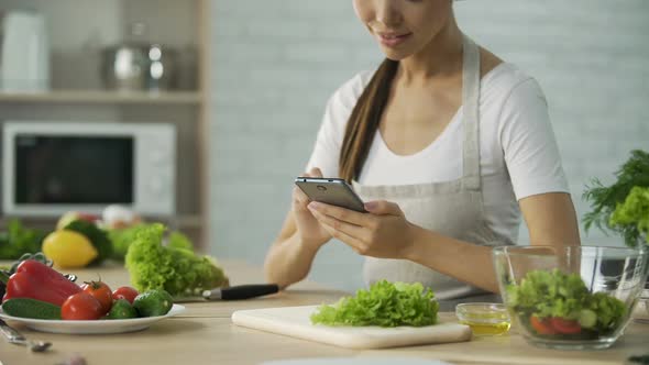 Attractive Female Sitting at The Table and Reading Salad Recipe on Cellphone