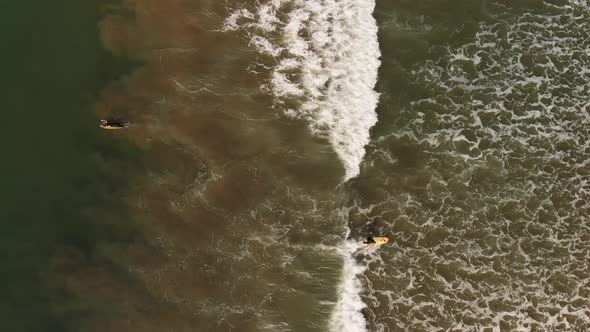 Aerial shot of two female surfers, one catching a wave in southern California