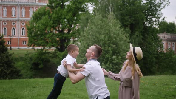 Father Throws Up His Hands Into the Sky Standing on a Green Meadow in Summer the Child's Mother is