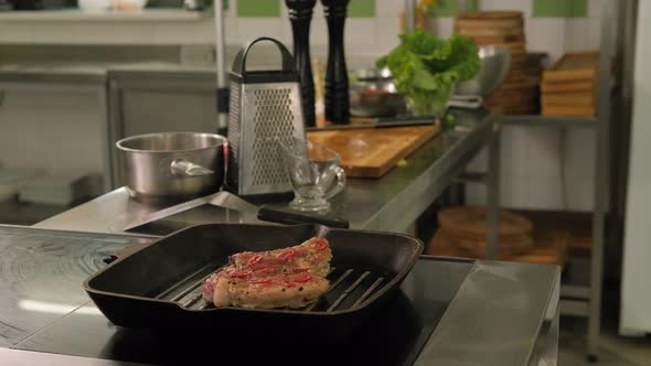 Closeup of a Chef Frying a Pork Steak on a Grill Pan in the Restaurant Kitchen