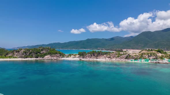 Drone flying over the crystal clear blue waters of Binh Tien Beach surrounded by green cliffs in Vie