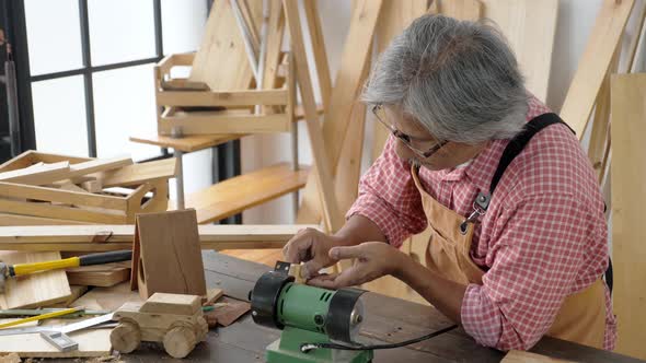 Senior Asian man making toy, doing woodwork.