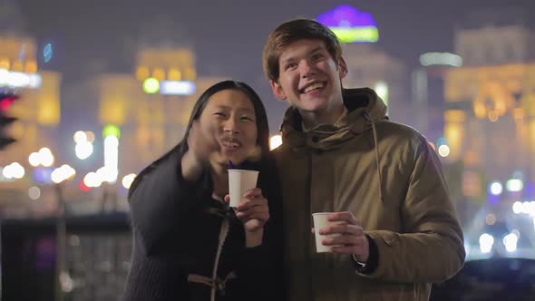 Young Happy Couple Enjoying Night Street Show, Drinking Tea, Having Fun Outdoors