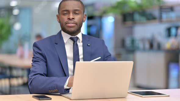 African Businessman with Laptop Looking at Camera in Cafe 