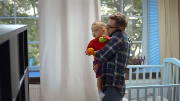 Busy Father Answering Phone Call with Toddler Son on His Arms