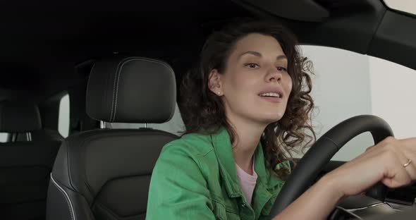 Young Beautiful Girl Chooses New Car at Car Dealership. The Woman Is Happy, Smiling and Rejoicing in