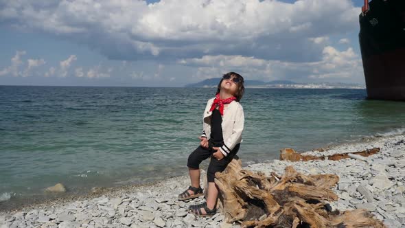 Stylish Child a Boy in a Black Jumpsuit and a Red Scarf Stands on the Beach