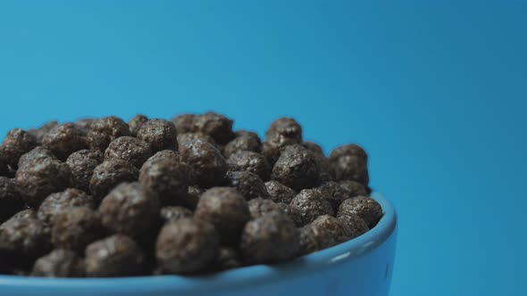 Chocolate breakfast cereals in balls are poured into a blue plate on a blue background