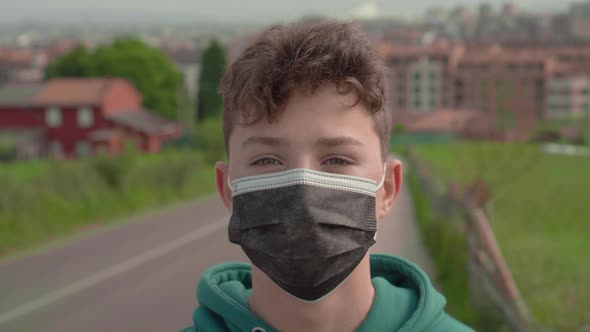 A young man in a black protective medical mask on the road in a suburban village