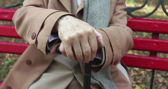 Close View of Tired Old Man's Hands Clutched on Crutch While Resting on a Bench