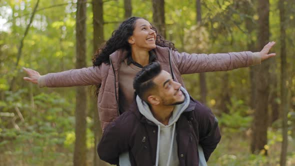 Young Guy Holding His Girlfriend Spinning Happy Girl Sits on Boyfriend's Back with Arms Out to Side