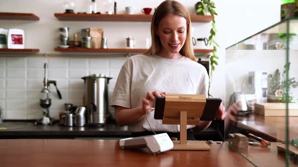 Smiling blonde woman barista punches the order at the checkout