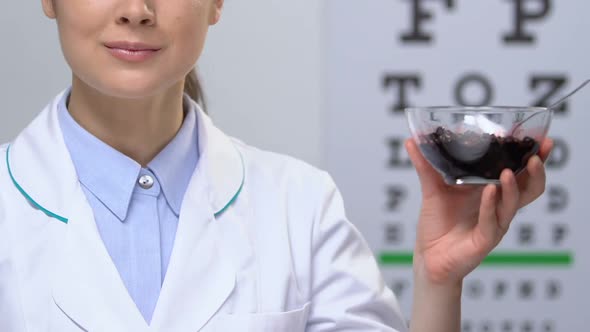 Female Doctor Showing Bilberry at Camera Against Eye Chart, Vision Health Care