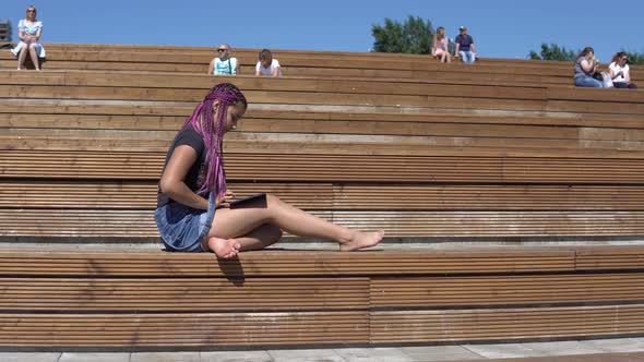 Young Girl Uses a Tablet Sitting on a Park Bench