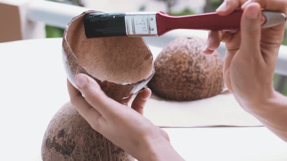 Female hands gently brushing sanded coconut shells with oil. Woman crafting coconut shells on balcon