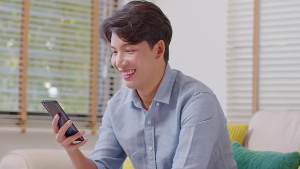 Millennial asian young man looking mobile phone laughing with good news