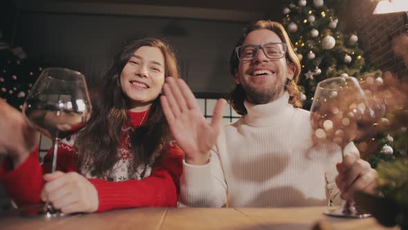 Young Couple Looking to Camera Waving Hands and Celebrating Xmas Via Video Chat on Laptop