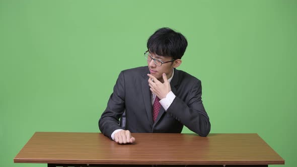Young Asian Businessman Bored and Tapping Fingers on Table